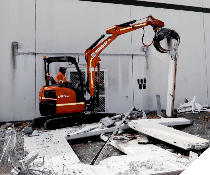 A mini excavator clearing out concrete walls removed by Slice It Right during an office strip out in Perth.